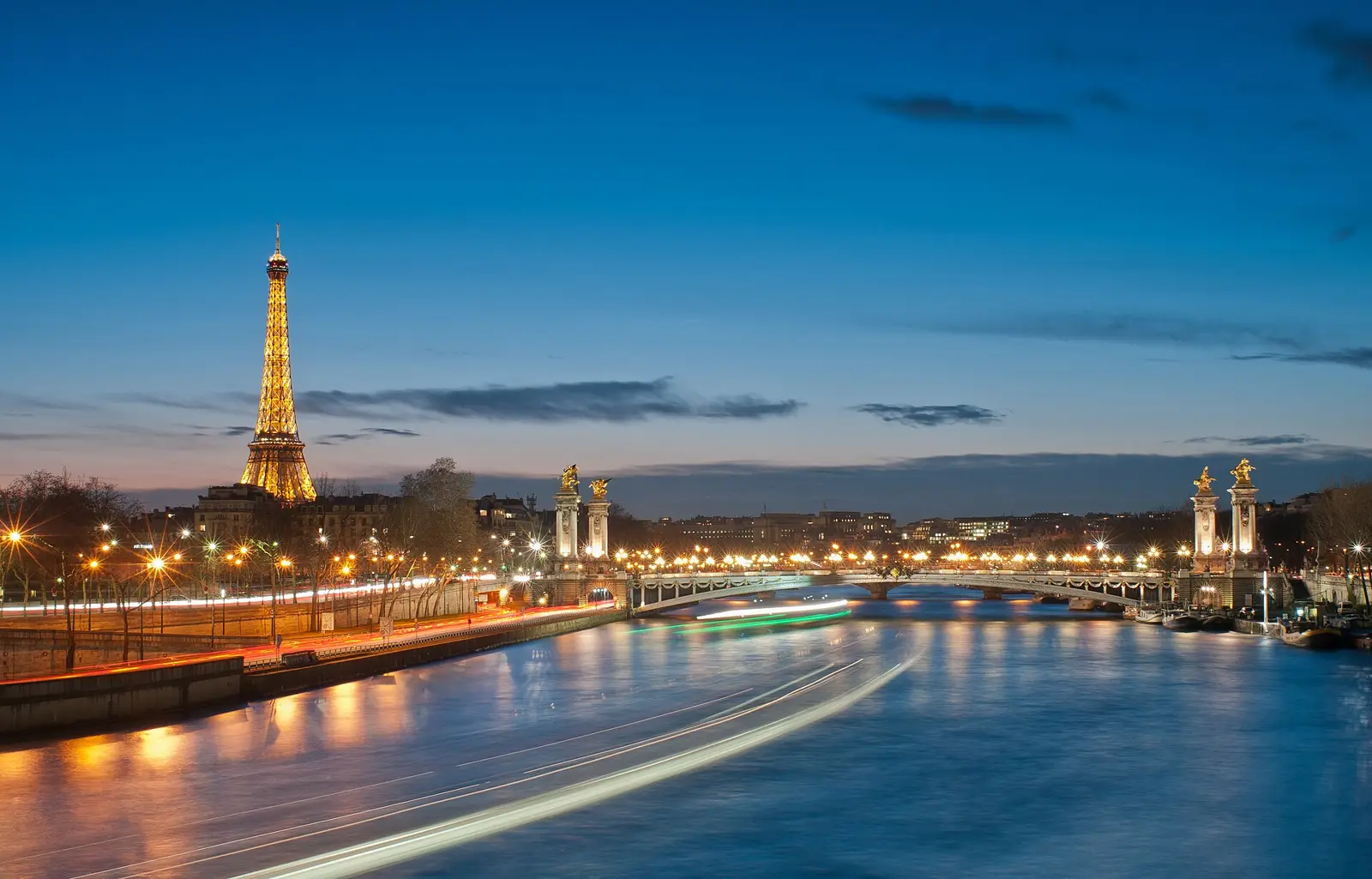 The Eiffel Tower lit up at night beyond the Pont Alexandre III.